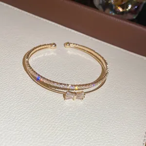 Detailaufnahme des goldenen zweilagigen Armreifs mit Zirkonia-Schleife und funkelnden Steinen.