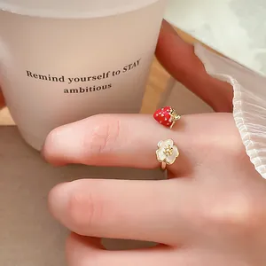 Primo piano di un anello aperto dorato con ciondoli a fragola e fiore bianco.