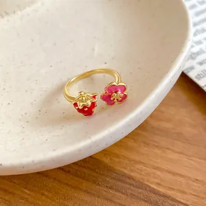 Primo piano dei ciondoli a fragola e fiore in smalto su un anello dorato aperto.