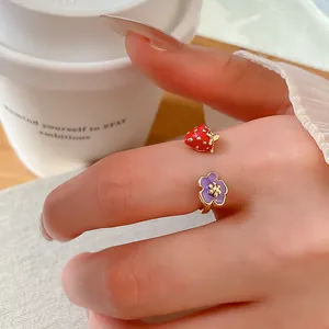 Primo piano di un anello regolabile in smalto con fragola e fiore sul dito.