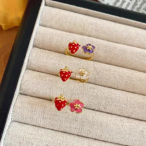 Dettaglio di anelli aperti con fragole e fiori in finitura dorata.