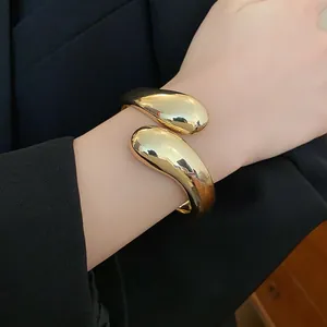 Primer plano de un brazalete abierto de gota de oro retorcido sobre una chaqueta negra
