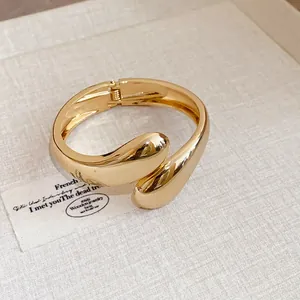 Brazalete abierto de gota de agua torcida dorada con un diseño minimalista y pulido