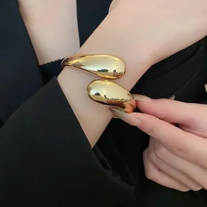 Vista detallada de un brazalete abierto dorado con forma de gota pulido puesto en la muñeca