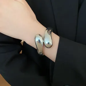 Detalle de un brazalete de gota de agua plateado retorcido en la muñeca sobre un traje negro.
