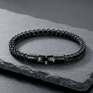 Detail view of a black stainless steel wheat chain bracelet on a slate stone background.