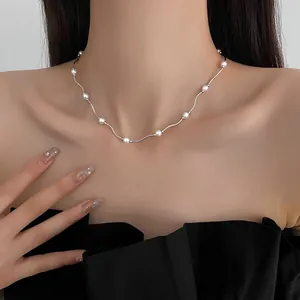 Close-up of minimalist wavy silver necklace with small white pearls on a model's collarbone