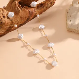 Close-up of minimalist white shell and pearl necklace on a delicate gold chain.