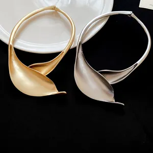Dettaglio di collari rigidi in metallo a forma di foglia oro e argento su fondo scuro.
