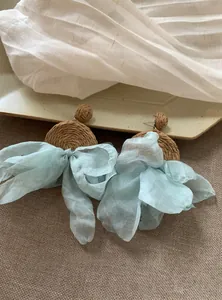Dettaglio degli orecchini pendenti in raffia intrecciata con fiocco in chiffon azzurro