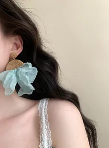 Dettaglio di orecchini pendenti in rafia e chiffon indossati da una modella chic