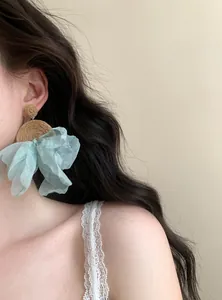 Vista dettagliata di orecchini pendenti boho in rafia e chiffon azzurro indossati da una modella