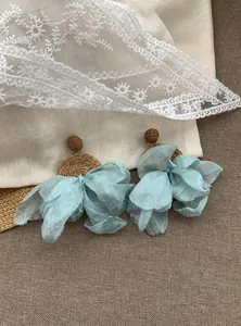 Dettaglio dei petali in chiffon blu e raffia intrecciata sugli orecchini pendenti