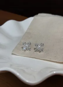 Close-up of elegant silver flower stud earrings with clear zircon stones on a canvas pouch