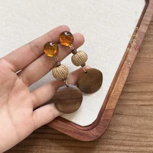 Dettaglio di orecchini etnici in legno con perle d'ambra e sfere di paglia intrecciata