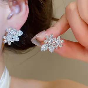 Detailed shot of sparkling zircon flower and leaf earrings on ear and held by hand