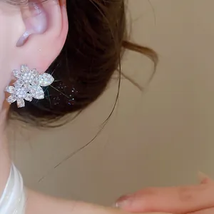 Close-up view of elegant silver needle zircon flower and leaf earrings on ear.