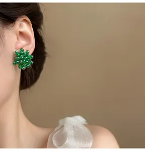 Primo piano di orecchini a perline verde scuro a forma di uva indossati da una modella