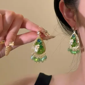 Vintage green resin drop earrings with floral details and beaded tassels on an Asian model