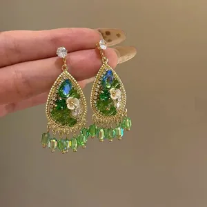 Macro view of vintage teardrop earrings featuring green crystals and resin flowers