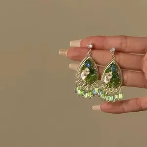 Close-up of vintage teardrop earrings with green resin beads and white floral detail