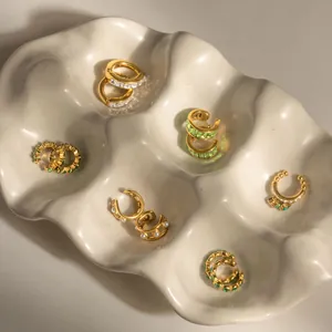 Detail view of assorted gold-plated ear cuffs with zircons and pearls on a ceramic tray