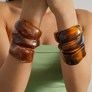 Detailed close-up view of chunky marbled amber acrylic bracelets worn on model wrists