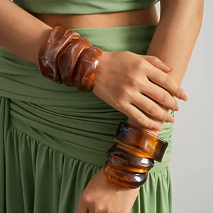 Close-up of chunky irregular amber acrylic bangles worn with a green dress