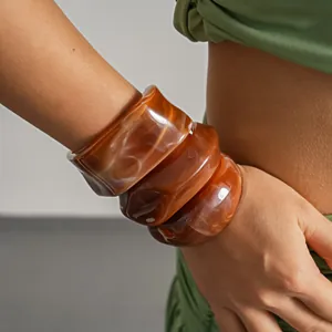 Detailed view of three irregular geometric amber acrylic marbled resin bangles on wrist