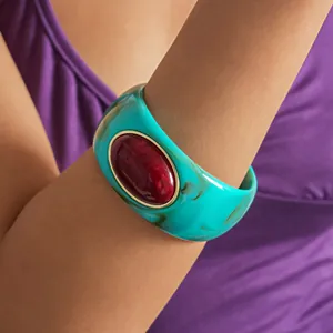 Close-up of a retro teal acrylic chunky bangle with a large oval red resin stone accent.