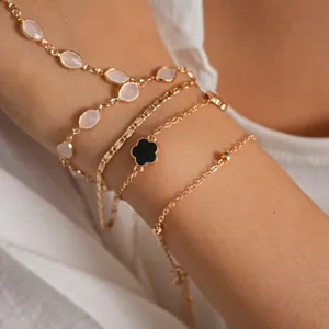 Detail view of gold-toned layered bracelets with black clover charm and resin beads