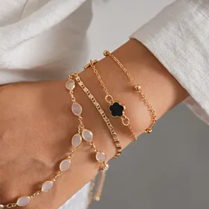 Close-up of a gold-tone bracelet set featuring pink resin beads and a black clover charm