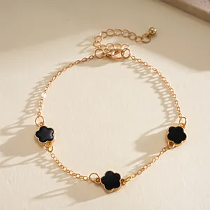 Elegant gold chain bracelet featuring three black flower charms on a textured surface