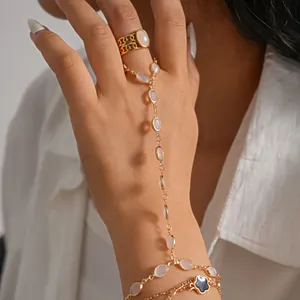 Close-up of elegant gold hand chain slave bracelet with white resin ovals and clover charm