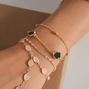 Close-up of elegant gold chain bracelets featuring pink resin beads and floral charms