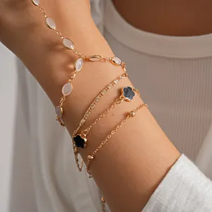 Close-up of gold layered bracelets with black clover and white resin beads