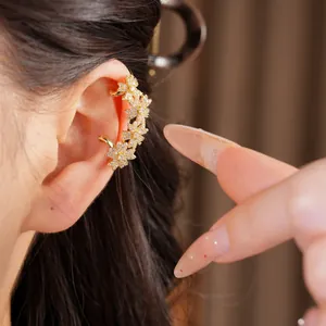 Close-up van een 14k vergulde zirkonia bloemen oormanchet op het oor van een model.
