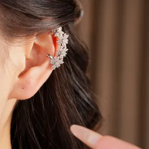 Detailopname van een 14k vergulde oormanchet met sprankelende zirkoonbloemen op het model