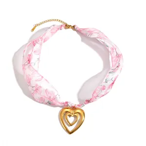 Close-up detail of a pink floral silk scarf necklace featuring a gold double heart pendant