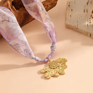 Macro view of golden sunflower pendant on a purple floral pattern scarf necklace.