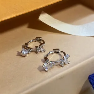 Close-up of silver-tone hoop earrings with zircon butterfly and square charms.