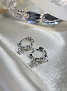 Detail view of silver hoop earrings with zircon butterfly and round pendants on silk.