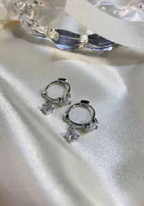 Detail view of silver hoop earrings with zircon butterfly and square stone charms.