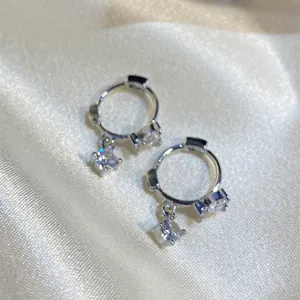 Close-up detail of silver hoop earrings with square zircon pendants on silk fabric