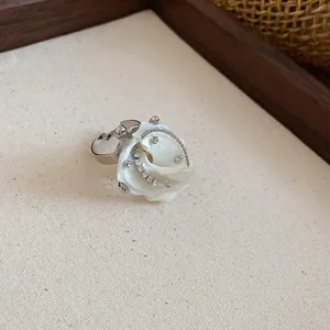 Close-up of a silver ring featuring a white shell-shaped flower with crystal accents