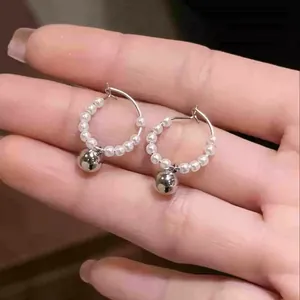 Detailed view of French-style hoop earrings with white pearls and silver ball pendant.