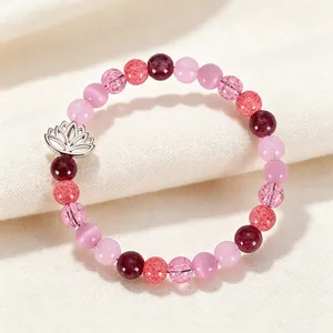 Detail view of a beaded bracelet with pink quartz, strawberry crystal, and a silver lotus charm.