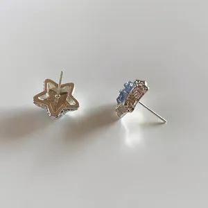 Macro view of silver-tone star stud earrings with light blue crystal inlay details.