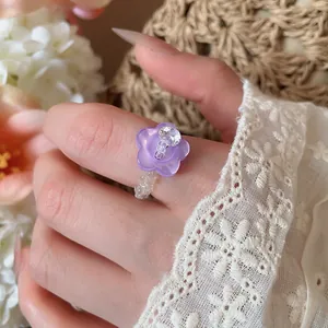 Dettaglio di un anello con perline, fiore viola e cristallo di zircone al dito