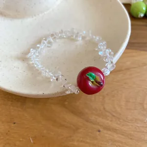 Macro dettaglio di un bracciale di perle di cristallo trasparente con ciondolo a mela.